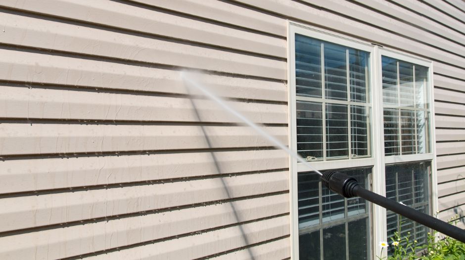 Pressure washing exterior house siding near a window